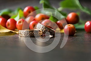 Rustic wedding decorations. Red small apples and gold rings on a wooden background with a blurry foreground with a place for an