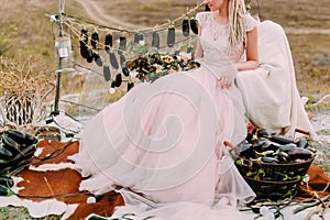 Rustic wedding in forest, bride sits in pink bridal dress near wedding decorations. Idea for eco wedding