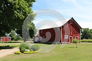 A rustic white tin roof red barn building with bright white trim and landscaped lawn and flower beds