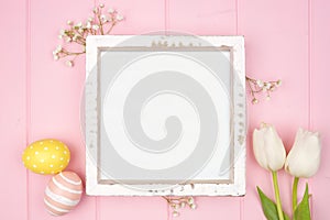 Rustic white wood frame with pastel Easter eggs and white spring tulip flowers. Top view against a pink wood background. Copy