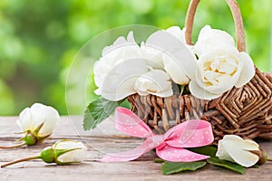 Rustic wicker basket with wild rose flowers and pink ribbon.