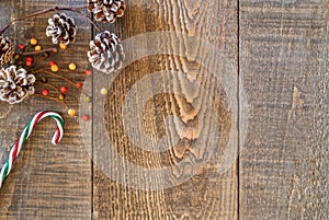 Rustic wood plank background with white tipped pine cones, berries and holiday candy cane on top left corner