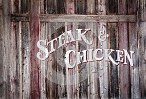 Rustic wood sign with steak and chicken painted on it.