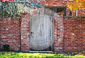 Rustic wooden arched garden fence in brick wall in autumn with colored leaves and brick house with colorful fall foliage reflected