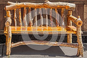 Rustic wooden bench made of rough logs with bark sitting on sidewalk against wooden wall on sidewalk