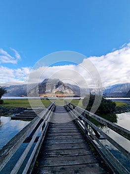 Rustic wooden bridge spanning a tranquil blue lake on a sunny day, providing a tranquil pathway