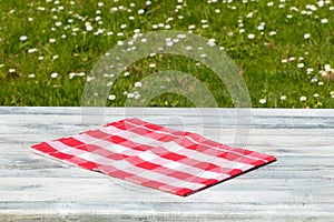 Rustic wooden bright table with beautiful spring meadow with daisies in background. Outdoor in morning. Space for products.