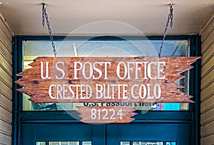 Rustic wooden sign for US Post Office Crested Butte CO handing by chain in front of door - some textured gunge