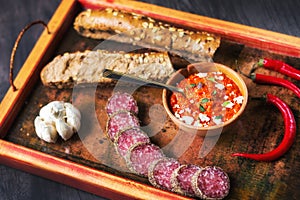 Rustic wooden tray with simple Balkan foods - ajvar spread, bread, meat, garlic and chilli peppers