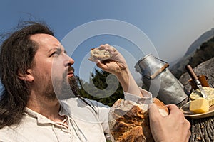 Rustically man with long hair eating bread in the nature