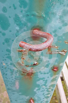 Rusting hook on green weathered post with oxidised metal erosion