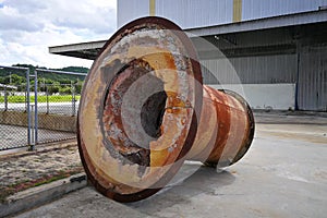 Rusting large machine part, placed outdoors in a factory area