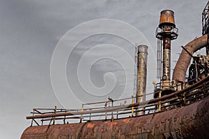 Rusting pipes with catwalks and railings, smokestacks in industrial complex