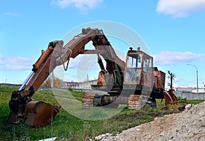 Rusty abandoned construction excavator with a bucket on the ground against the blue sky