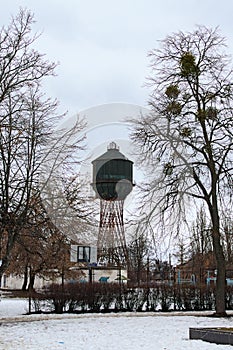 Rusty abandoned water tank in Bila Tserkva. Tree leaves border. Natural frame. Bare trees and snow on the ground in city park