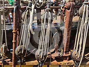 Rusty anchor is anchored between the wooden blocks and the rigging of an old sailing ship