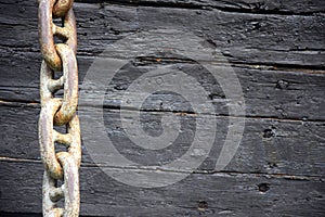 Rusty anchor chain on the background of an old wooden decorative ship