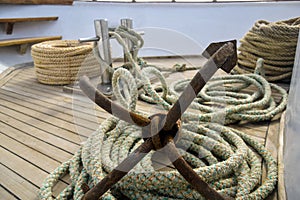 Rusty anchor with coiled rope lies on wooden deck of yacht. Auxiliary yacht equipment. Copy space. Close-up.