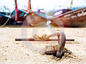 Rusty anchor on the sand beach with traditional long tail boat