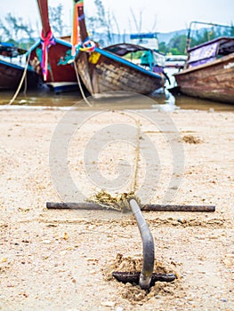 Rusty anchor on the sand beach with traditional long tail boat