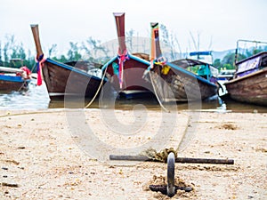 Rusty anchor on the sand beach with traditional long tail boat
