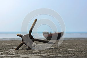 Rusty anchor on a wet beach with traditional country boat in background