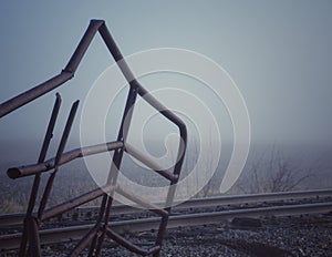 Rusty bent metal fence near railroad tracks in the fog.