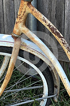 Rusty bicycle frame resting against a wood fence