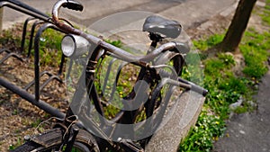 Rusty bicycle with light lamp parked by asphalt sidewalk