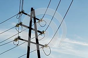 A rusty black power line with bright glass insulators on the blue sky with white clouds background