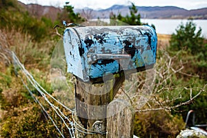 A rusty blue mailbox on the side of a road in remote scottish village