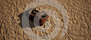 Rusty brown jerrycan lying in rippled sand of beach.