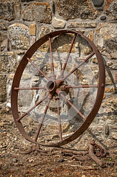 Rusty cart wheel resting against a stone wall