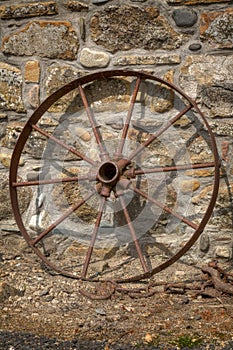 Rusty cart wheel resting against a stone wall no. 2