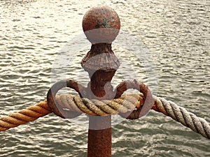 A rusty cast metal bollard with a gross hawser.
