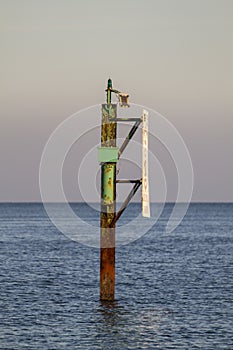 Rusty channel marker pole in water on sunny winters day
