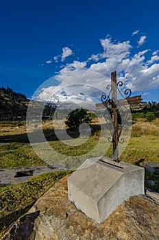 rusty cross on rock in yungay cemetery in foreground with snowy mountain in the background
