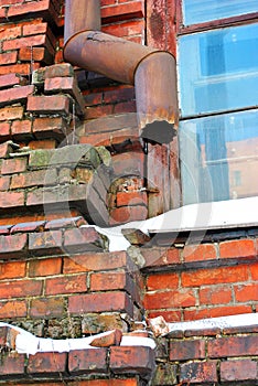 Rusty drain pipe along window corner on red brick wall, snow on window sill