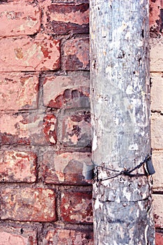 Rusty drain pipe with coiled wire on red brick wall