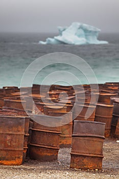 Rusty drums on Arctic coast with iceberg on background