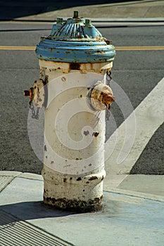 Rusty firehydrant with aged and weathered exterior white and aqua green color on side of urban street corner