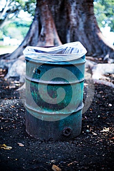 Rusty garbage can in front of a tree in a public park
