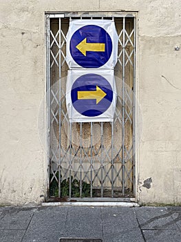 a rusty gate with a metal grille, with two contradictory traffic signs of obligatory direction, sense of contradiction or