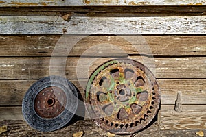 A rusty gear and brake rotor leaning against the wall of an old wood building