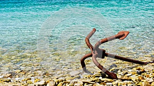 A rusty grapnel anchor lying on its side on shore.