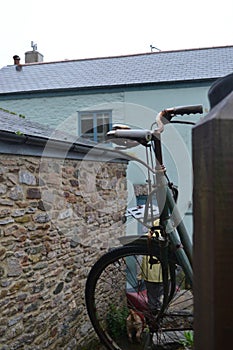 Rusty green bike propped up in a house`s backyard in the rain