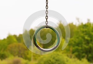 A rusty gymnastic ring on the street in a recreation park. Close-up of an old hanging ring against a background of blurred trees.