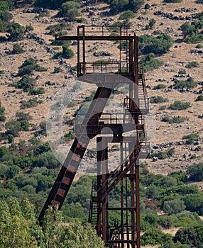 Rusty industrial tower stands isolated against a dry hillside covered
