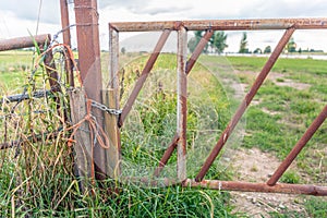 Rusty iron gate closed with a knotted orange rope and a steel ch