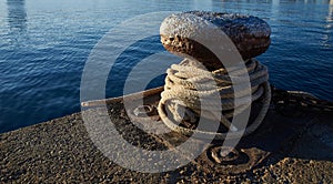 Rusty iron mooring bollard with nuatical ropes.